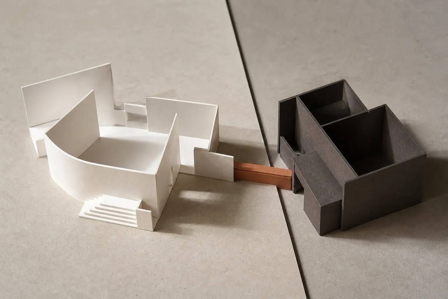 An open cream paper structure and a sheltered charcoal structure joined by one terracotta passage.